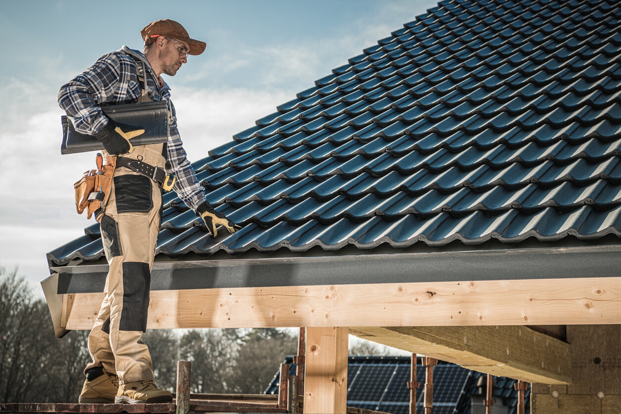 A male roofer standing on a ladder next to a newly installed black roof.