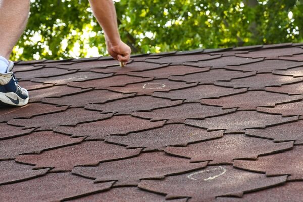A roofer draws circles around problem areas in a homeowner's roof. This roof inspection can help with insurance claims.