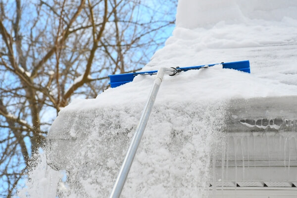 A homeowner tries to clean their gutters after an ice dam has formed on their roof in the winter. 